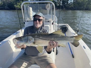 An angler proudly displaying a large Snook while seated on a boat in a scenic fishing environment.