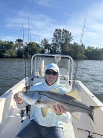 Angler proudly displaying a large Snook while seated in a boat, surrounded by a scenic waterway.