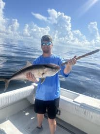 Angler proudly displaying a large fish while aboard a boat in clear waters, showcasing a beautiful day for fishing.