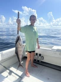 An angler proudly displaying a large Amberjack while fishing on a sunny day in open waters.