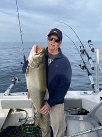 An angler proudly displaying a large Lake Trout while fishing on a boat in open waters.