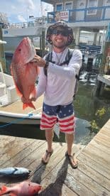 Angler proudly displaying a large Red Snapper on the dock after a successful fishing trip.