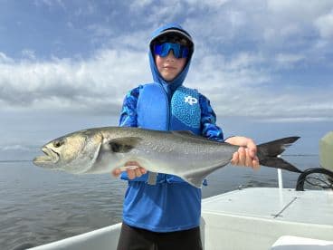 Young angler proudly holding a large Snook while fishing on calm waters.