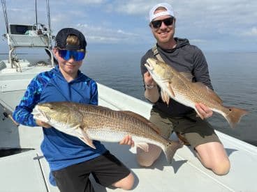 A young angler and an adult proudly displaying their Redfish catch while fishing on a calm day.