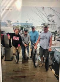 A group of four anglers proudly displaying their catch of large tuna at the marina, showcasing a successful fishing trip.