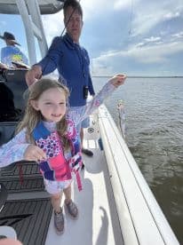 A young girl in a life jacket proudly displays her catch while fishing on a boat, showcasing a successful day on the water.