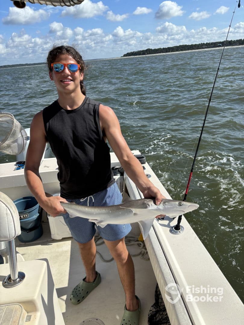 Young angler proudly holding a small shark while fishing on a boat, showcasing a sunny day on the water.