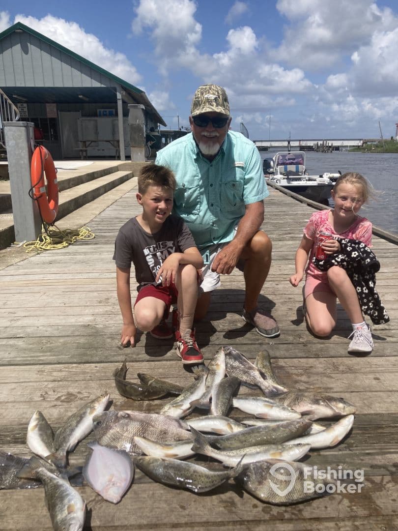 A family poses with a variety of fish, including Speckled Trout, on a dock after a successful fishing trip.