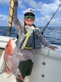 A young angler proudly displaying a vibrant Red Snapper while fishing on a boat in open waters.