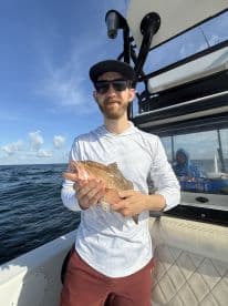 An angler proudly displaying a Grouper while fishing offshore, with a scenic ocean backdrop.