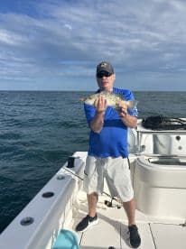 An angler proudly displaying a Speckled Trout while fishing on a boat in open waters.