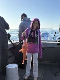 A young angler proudly displaying a vibrant red rockfish while fishing on a boat, showcasing a joyful moment on the water.