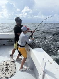 A young angler and an adult are engaged in fishing on a boat, with the child actively reeling in a catch in a scenic ocean setting.