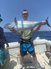 An angler proudly displaying a large fish on a fishing boat, showcasing a successful deep-sea fishing trip.