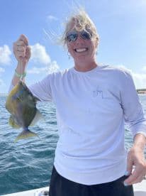 An angler proudly displaying a colorful fish while enjoying a sunny day on the water, showcasing a successful catch during a fishing trip.