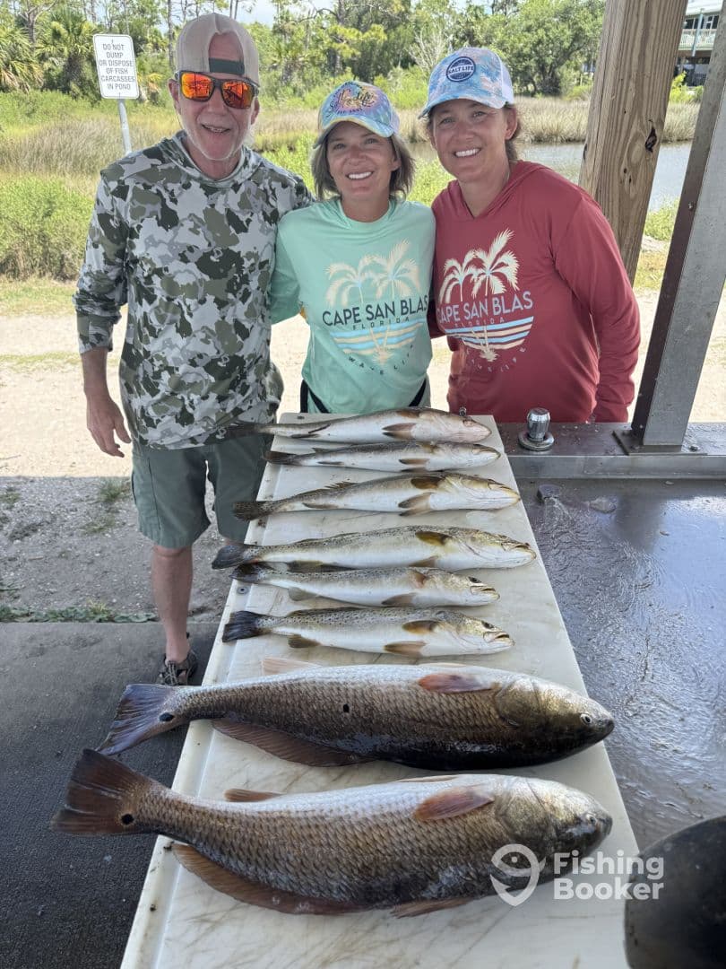 A group of anglers proudly displaying their catch of Redfish and Speckled Trout on a cleaning table after a successful fishing trip in Cape San Blas.
