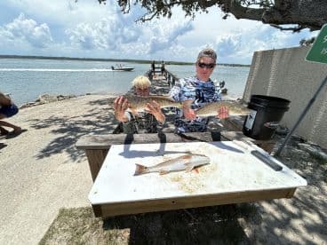 Two young anglers proudly displaying their catch of Redfish at a dock, showcasing a successful day of fishing in a coastal environment.