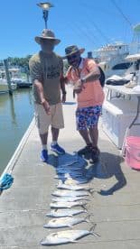 Two anglers proudly displaying a catch of several Spanish Mackerel on the dock after a successful fishing trip.