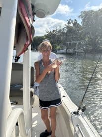 An angler proudly displaying a freshly caught fish while aboard a boat in a scenic waterway.