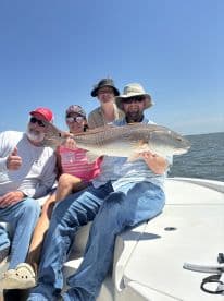 A family proudly displaying a large Redfish while enjoying a sunny day on the water.