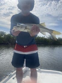 Angler proudly displaying a Snook while fishing from a boat in a scenic coastal environment.