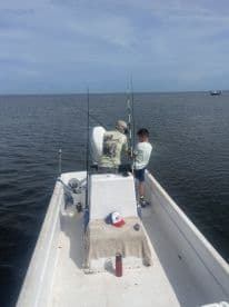 A young boy and an adult are fishing together on a small boat, enjoying a day on the water with multiple fishing rods set up.