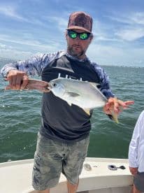 An angler proudly displaying a Silver Pompano while fishing on a boat, with a scenic backdrop of water and sky.