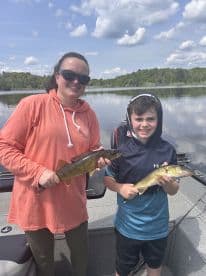 A mother and son proudly displaying their Walleye catch while fishing on a serene lake.