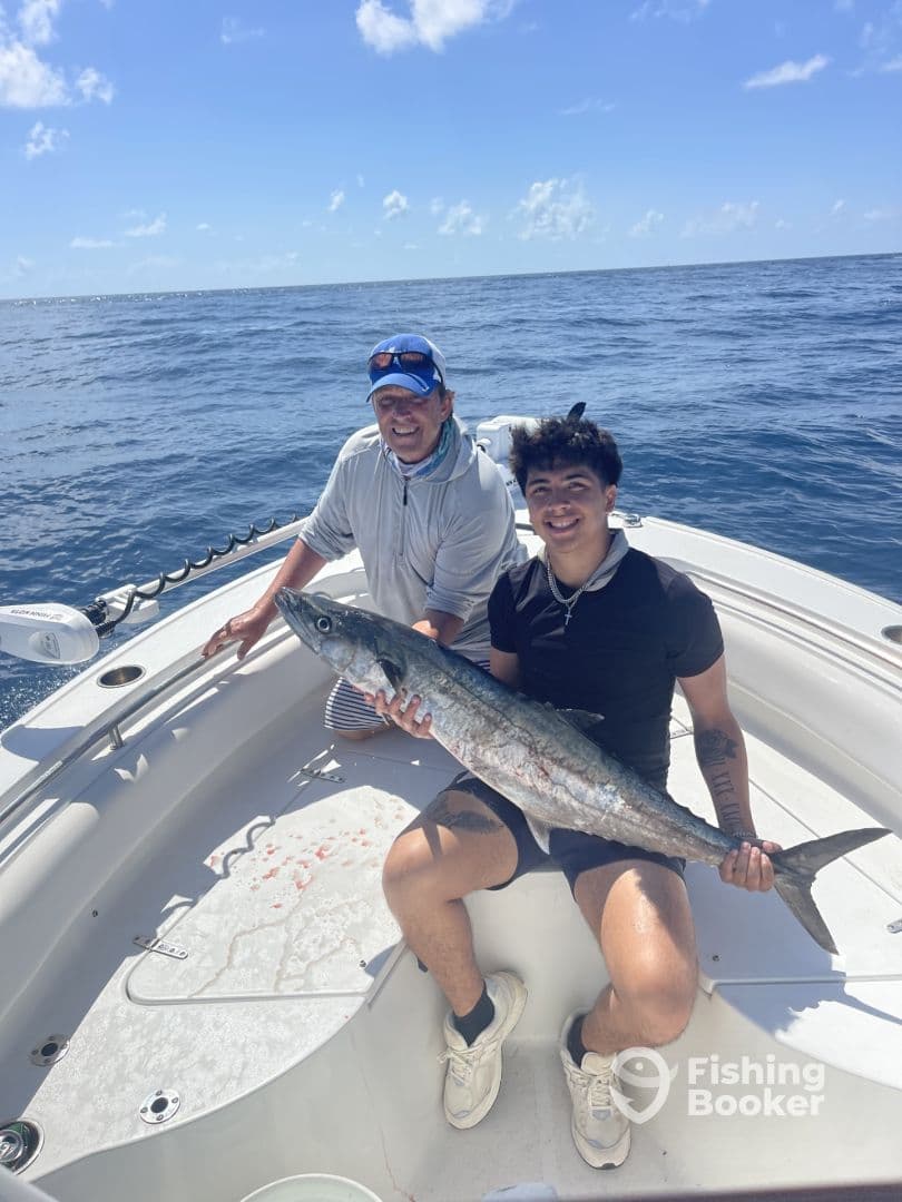 Two anglers aboard a boat proudly displaying a large King Mackerel caught during a deep-sea fishing trip.