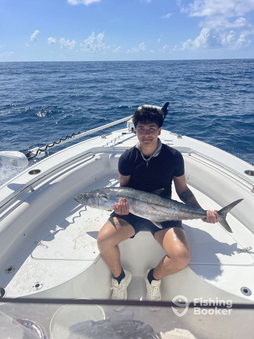 A young angler proudly displaying a large King Mackerel while seated on a boat in open waters.