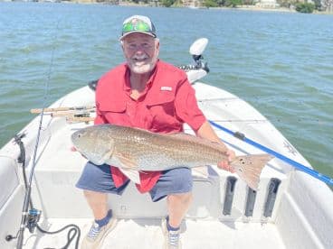 An angler proudly displaying a large Redfish while fishing on a sunny day in a coastal waterway.