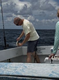 A fisherman is actively reeling in a catch on a boat in open water, showcasing the excitement of the fishing experience.