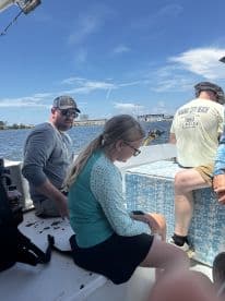 A family enjoying their time on a fishing boat, with a young girl seated and focused, while adults relax nearby, showcasing a casual fishing trip atmosphere.