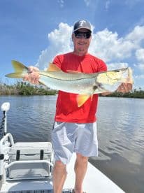 An angler proudly displaying a large Snook while fishing on a sunny day in a calm waterway.