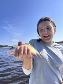 A young angler joyfully holding a colorful fish while fishing on a sunny day, showcasing a successful catch.