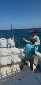A young angler and an adult are actively fishing on a boat, with the ocean in the background, showcasing a dynamic fishing moment.