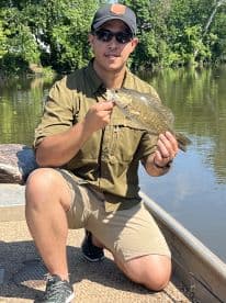 Angler showcasing a freshly caught Smallmouth Bass while fishing on a calm river, enjoying a sunny day on the water.