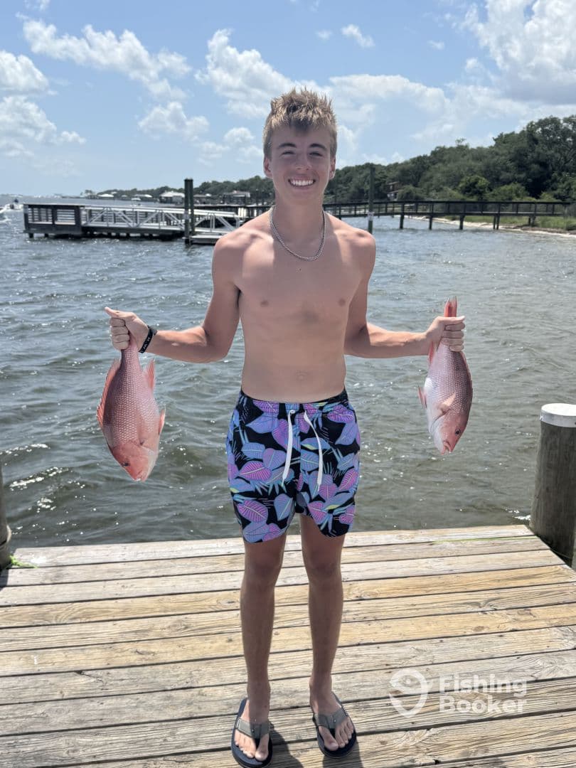 A young angler proudly displaying two Red Snapper at the dock, showcasing a successful fishing trip.