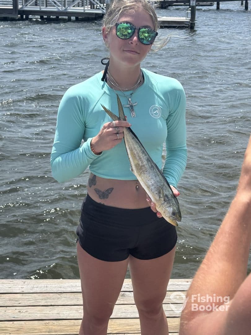 Young angler proudly displaying a caught fish at the dock, showcasing a sunny day on the water.