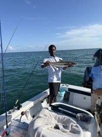 A young angler proudly displaying a large fish aboard a fishing boat in open waters, showcasing a successful day of fishing.