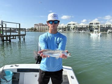 A young angler proudly displaying a Speckled Trout while fishing from a boat in a coastal waterway.