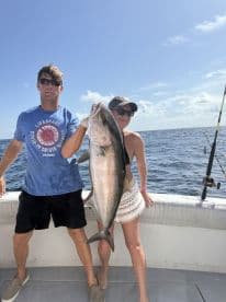 Two anglers proudly displaying a large Amberjack while on a fishing charter in open waters.