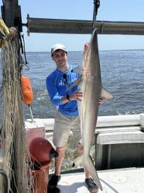 Angler proudly displaying a large shark caught during a fishing trip on a boat, showcasing the excitement of deep-sea fishing.