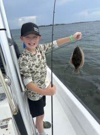 A young angler proudly displaying a Flounder while fishing on a boat, showcasing a fun day on the water.