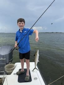 A young angler proudly displaying a Speckled Trout while fishing from a boat in a coastal waterway.