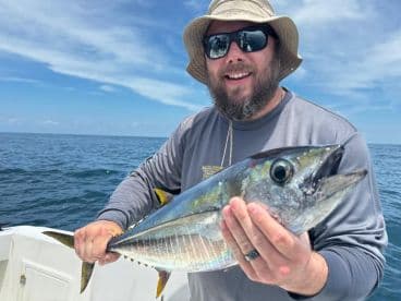 An angler proudly displaying a large Yellowfin Tuna while fishing offshore, showcasing a sunny day on the water.