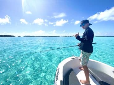 A young angler enjoying a fishing adventure on a clear blue ocean, casting from a small boat under a sunny sky.