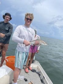 A young angler proudly displaying a shark caught during a fishing trip, surrounded by friends on a boat.