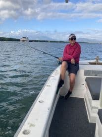 A woman enjoying a relaxing moment while fishing on a boat, with a scenic view of the water and distant hills.
