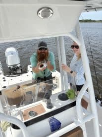 Two anglers aboard a boat, with one proudly displaying a fish while the other smiles, showcasing a fun fishing experience.
